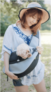 一名婦女抱著一隻裝在斜背包裡的狗。