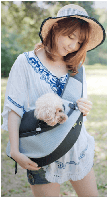 一名婦女抱著一隻裝在斜背包裡的狗。