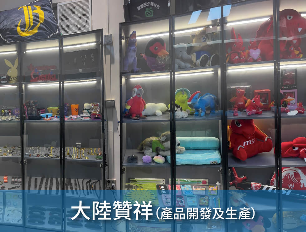 一個陳列櫃,裡面裝滿了毛絨玩具、公仔和品牌商品,例如帽子和鑰匙扣。底部的藍色橫幅上的中文文字是"大陸贊祥(產品開發及生產).